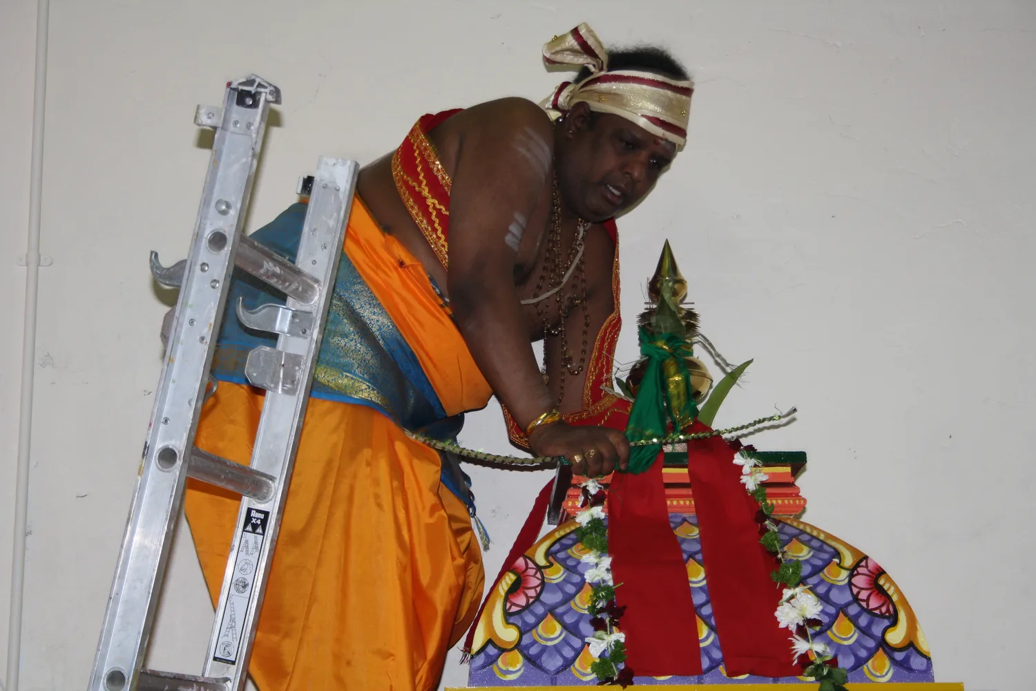 A priest on the ladder at the tower, setting the finial in place.