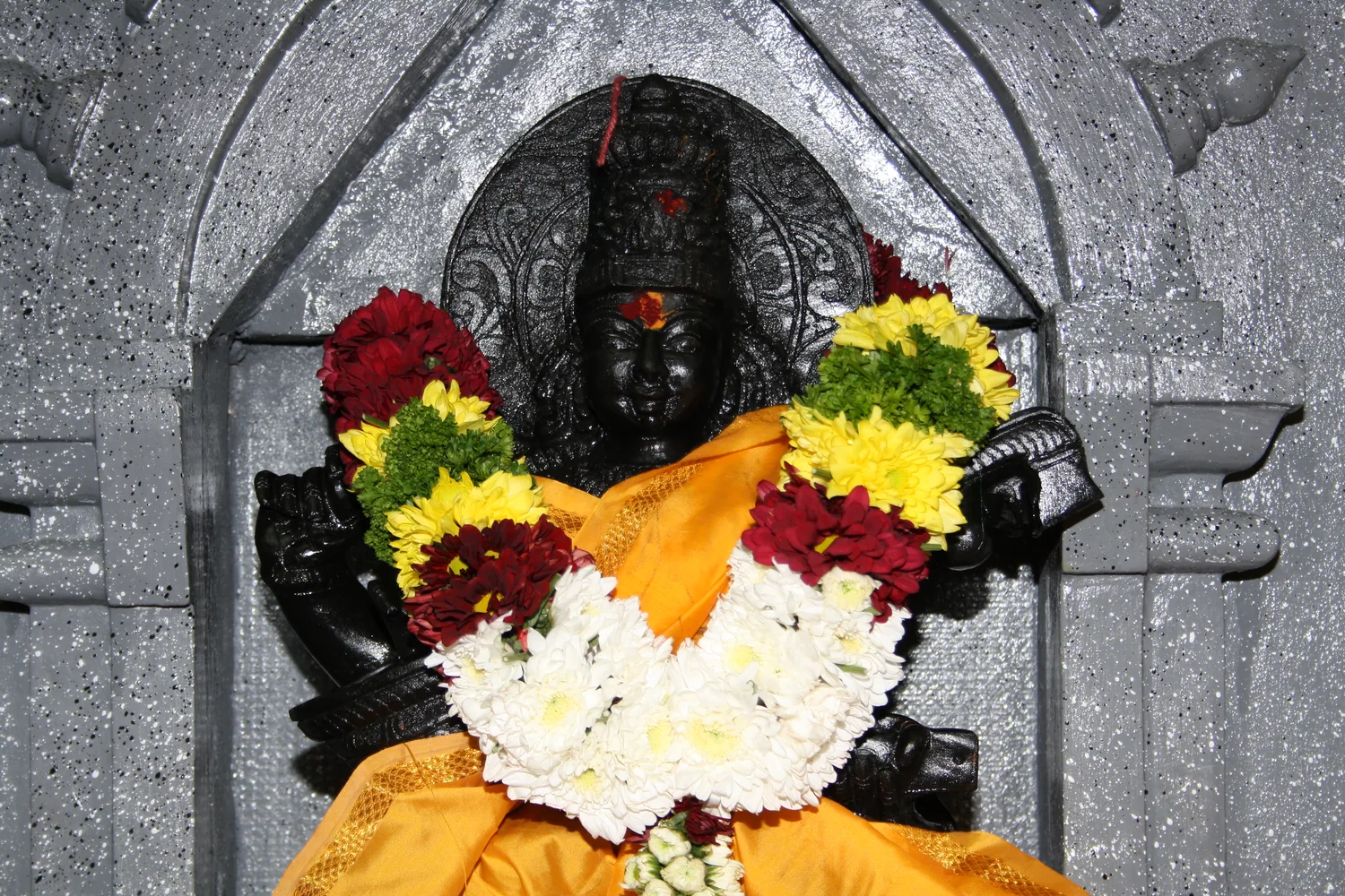 A garlanded deity deep in the granite niche.