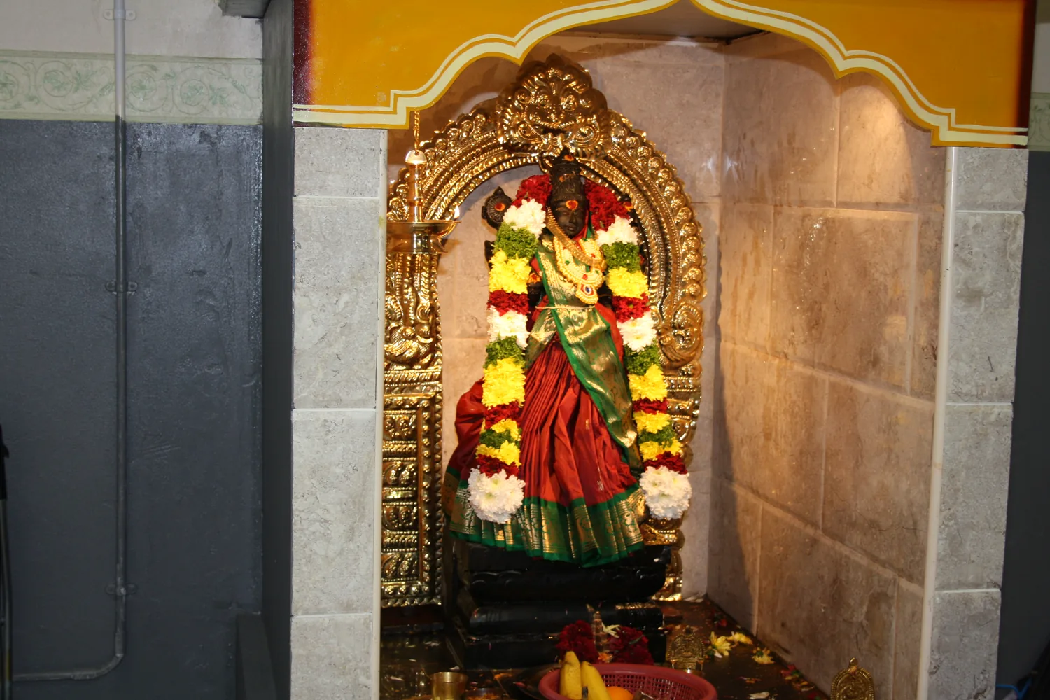 A garlanded deity in the granite niche.